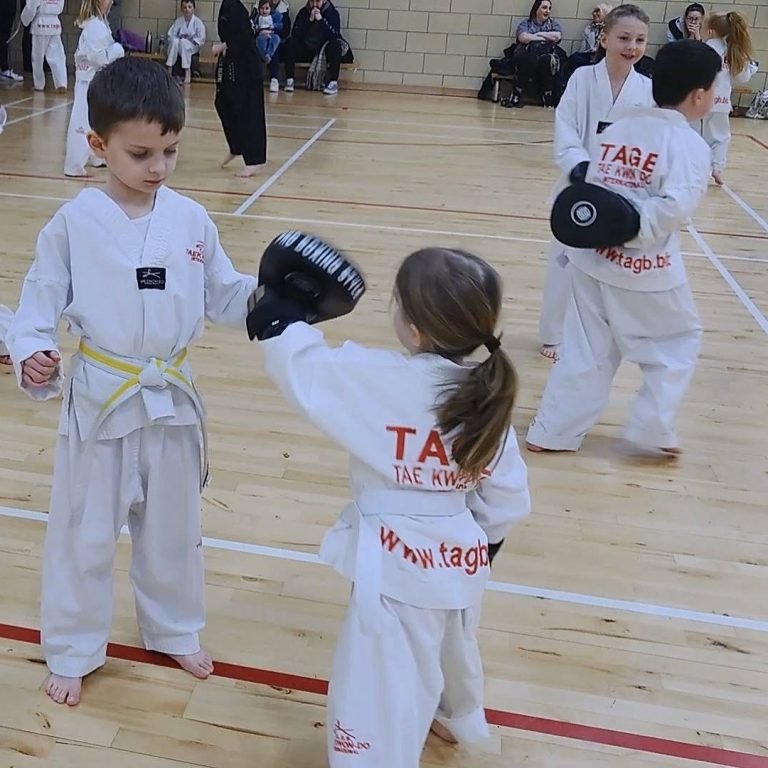 Kids Classes from 5 Years Old Children in martial arts uniforms practice sparring in a gym setting.