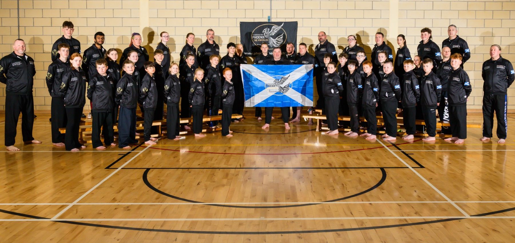 Scottish TaeKwon-Do Team 2024 World Championships Group of martial artists in black uniforms, posing with a Scottish flag in a sports hall.