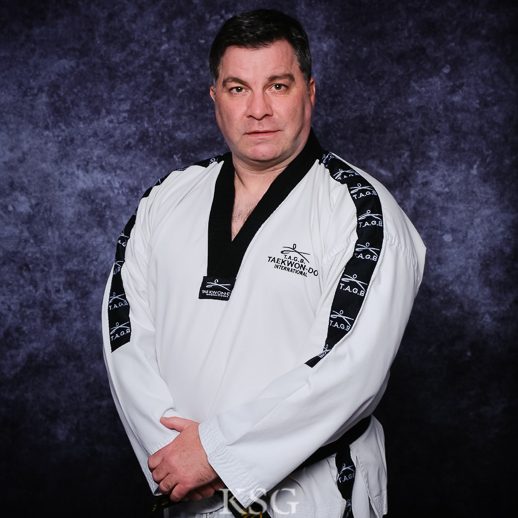 Master Scott McMillan Master Scott McMillan in a white taekwondo uniform standing confidently against a dark background.